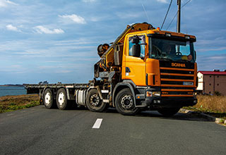 macara portocalie fassi montata pe un camion scania oprita o pe strada cu operatorl a volan