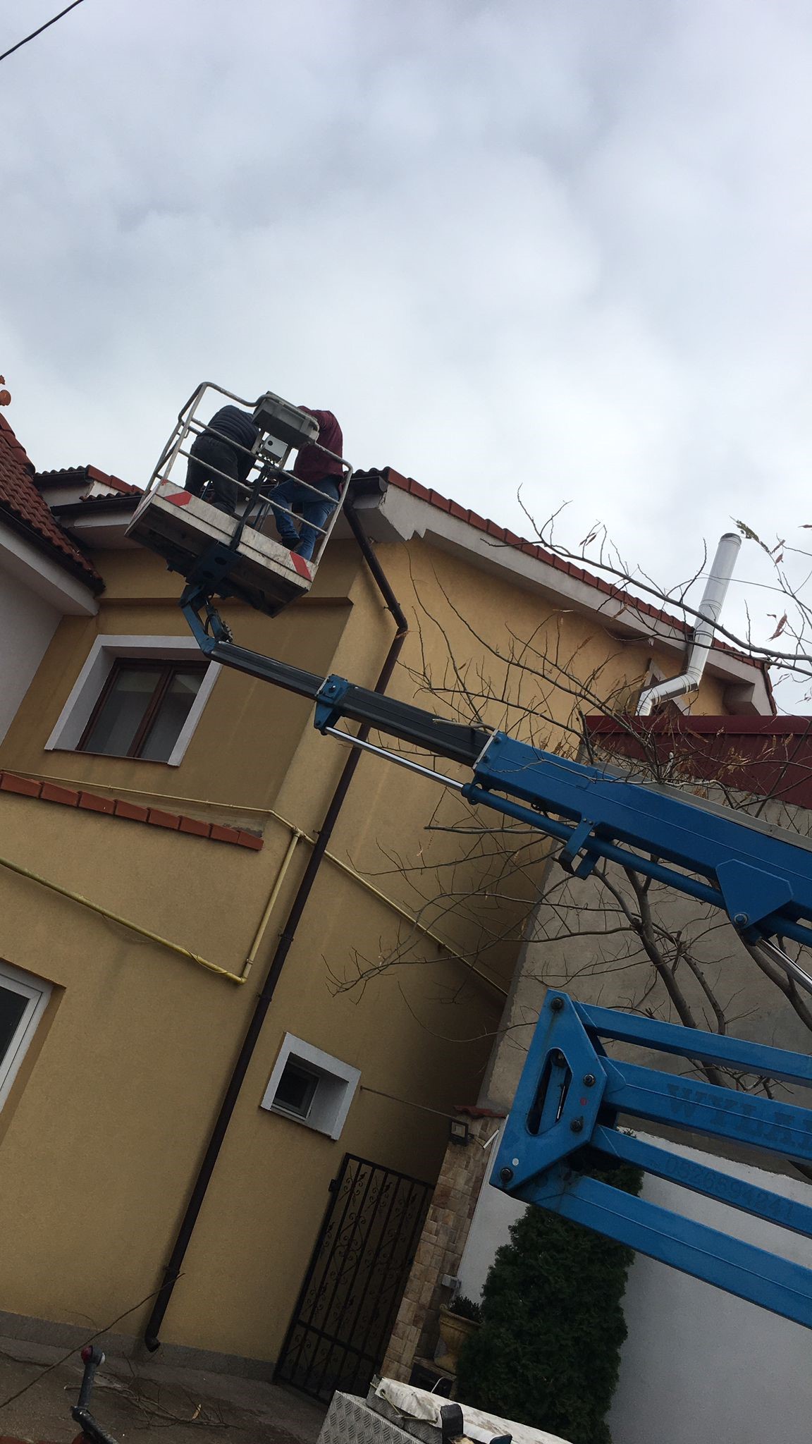 blue truck mounted boom lift and two people working on house roofing